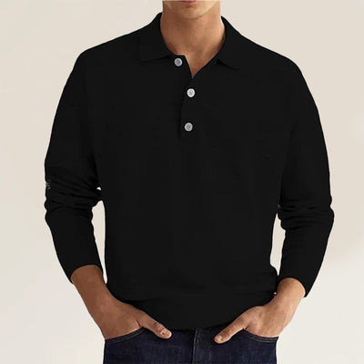 A man sporting a black polo sweater paired with dark jeans.
