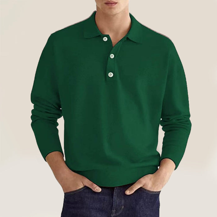 A man dressed in a dark green polo sweater paired with denim jeans.