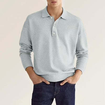 A man in a light blue polo sweater styled with jeans.
