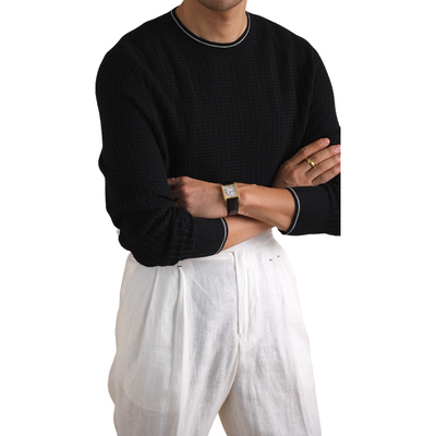 Men's black knit sweater paired with white pleated trousers.