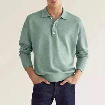 A man wearing a mint green polo sweater with dark jeans.