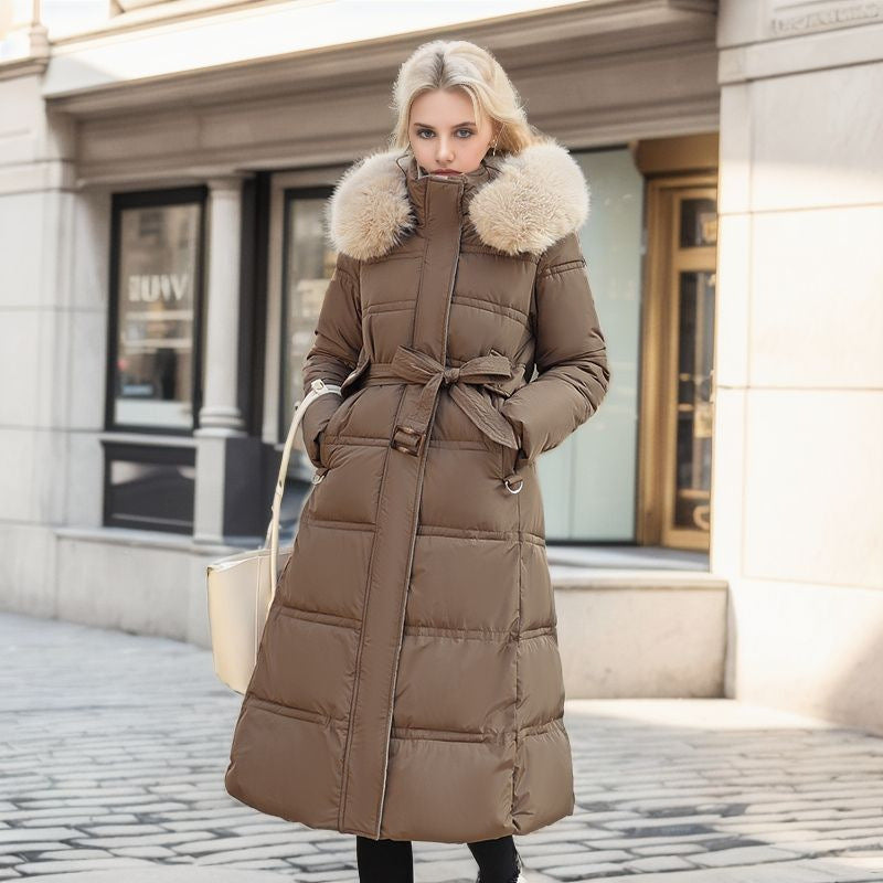 A woman dressed in a brown down coat featuring a fur collar, smiling while enjoying the chilly weather.